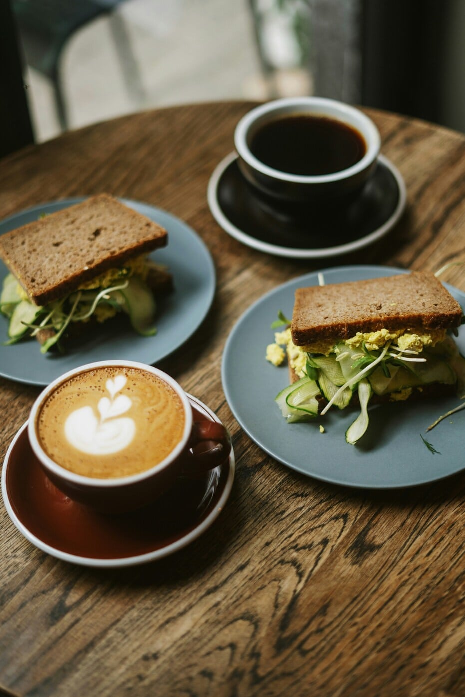 Vegan tofu scramble sandwiches with cucumber and coffee on a wooden café table