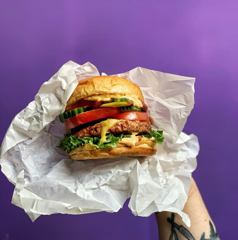 Vegan burger in a paper wrap held in front of a purple wall, example of the best vegan burgers in the UK